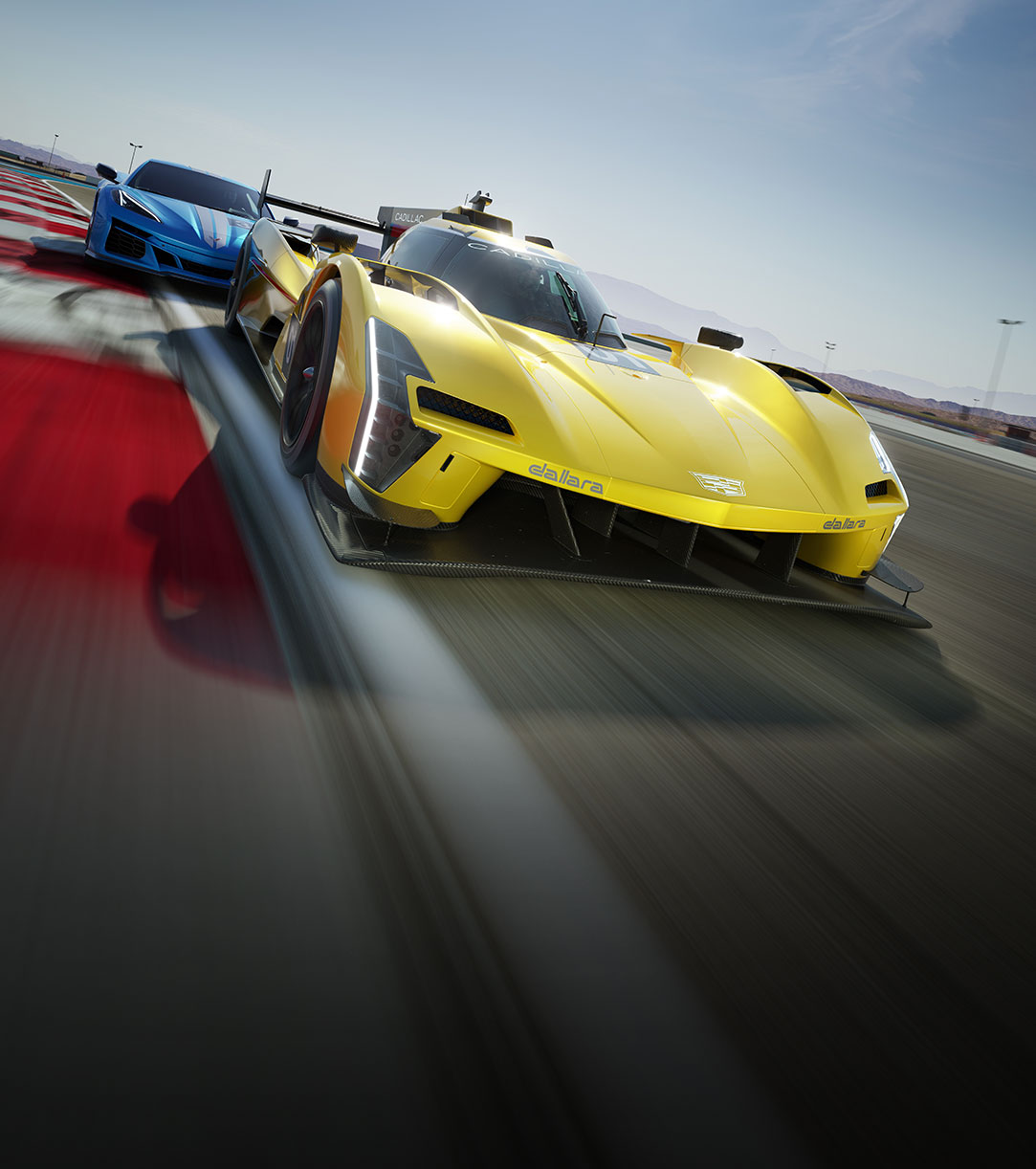 A yellow racing car followed closely by a blue racing car speeding down a track on a clear day. 