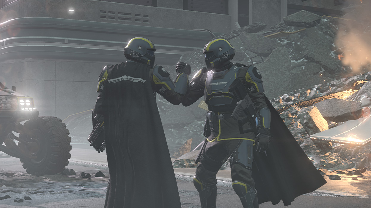 Two Helldivers grasping hands in front of a pile of rubble.