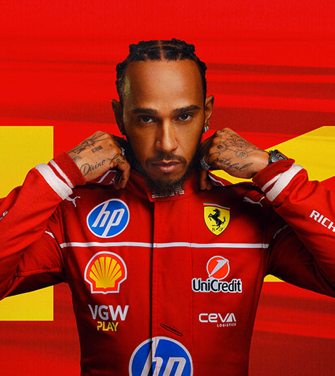 British Formula One racing driver Lewis Hamilton poses in a red racing suit in front of a red #44 flag.