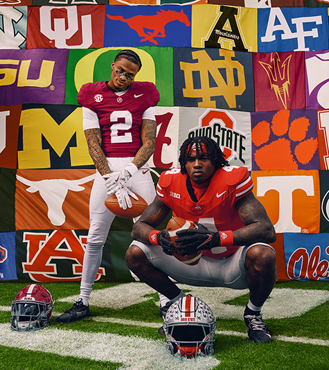 American football players posing on a football field in front of a banner featuring dozens of US college team logos.