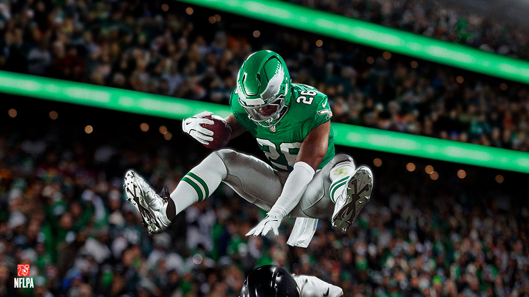 A Philadelphia Eagles football player leaping over another player with a football in hand.