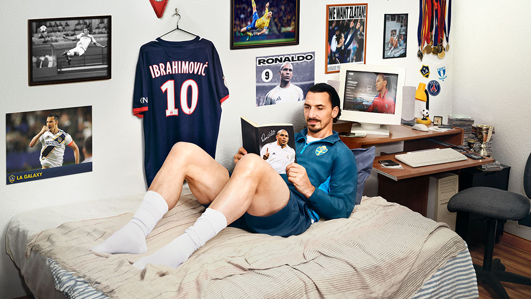A soccer player lounging in his bed reading a magazine.
