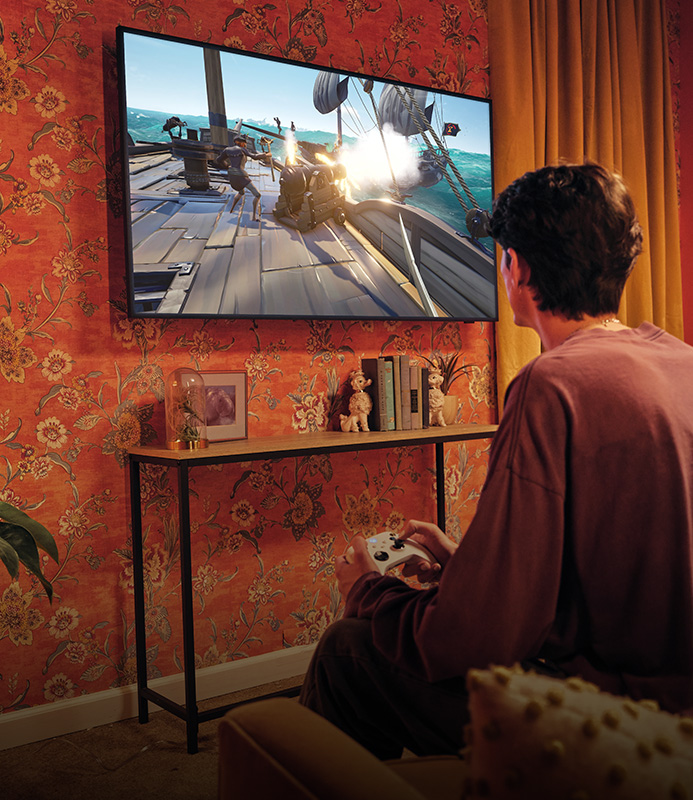 A person sitting in a chair with an Xbox Wireless Controller in hand playing an Xbox game on their TV without a console.