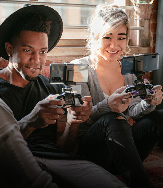 Two people sitting on a couch playing games on their phone using a gaming mobile clip. 