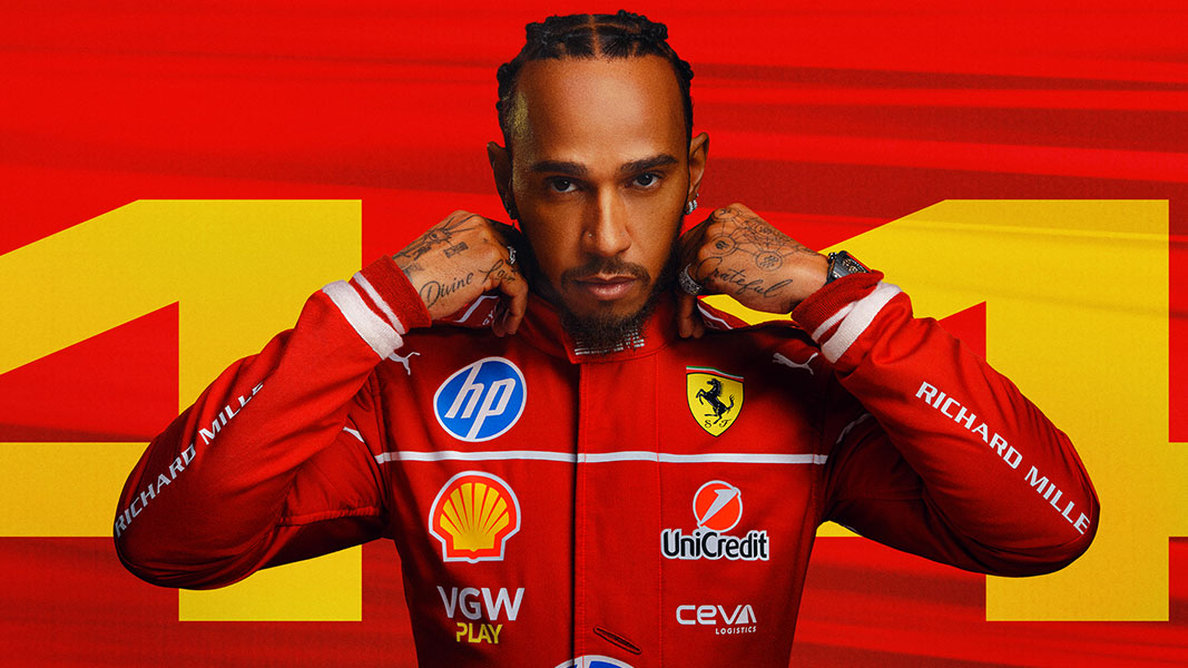 British Formula One racing driver Lewis Hamilton poses in a red racing suit in front of a red #44 flag.