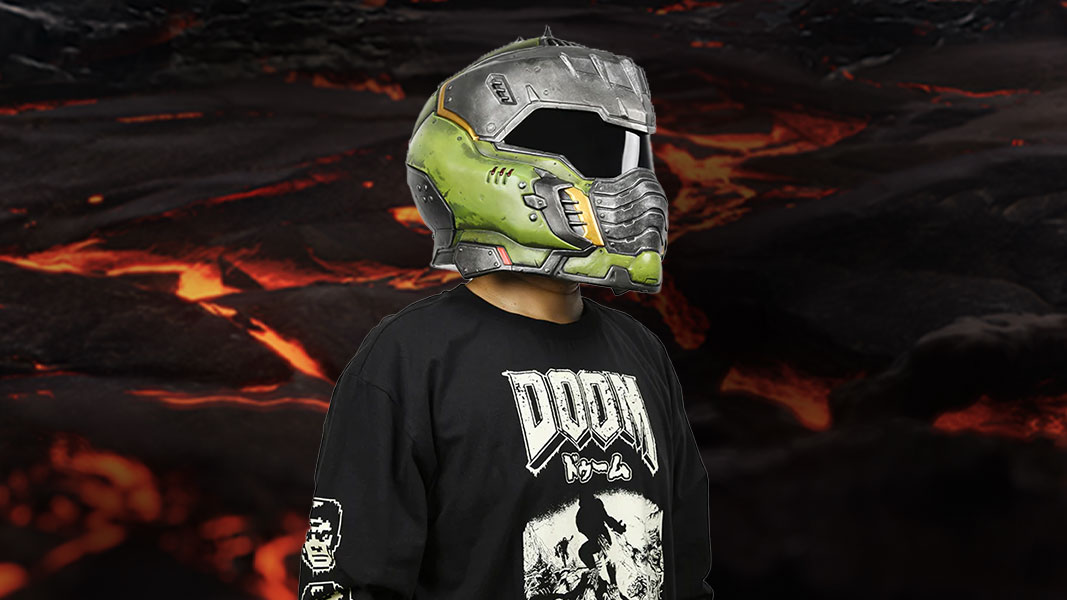 A person wearing a green and silver DOOM: The Dark Ages helmet and DOOM t-shirt