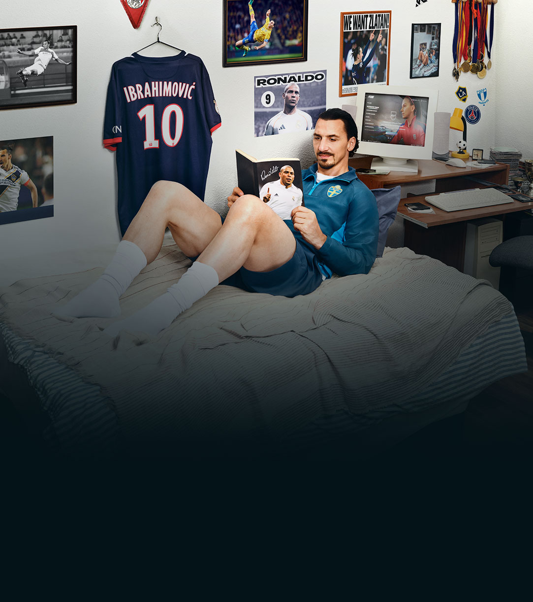 A soccer player lounging in his bed reading a magazine.