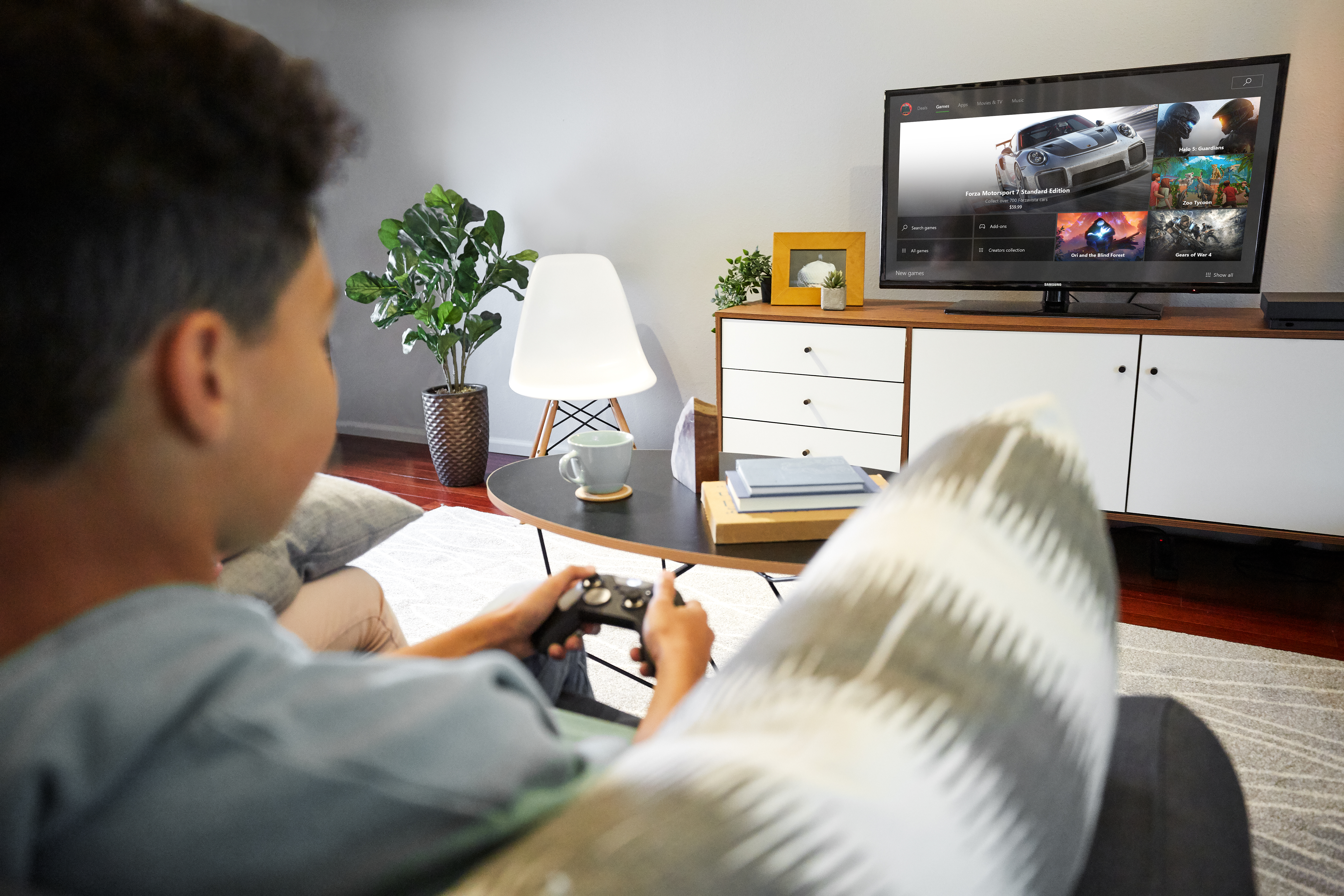 A young player uses an Xbox controller to browse Xbox games on his TV monitor.