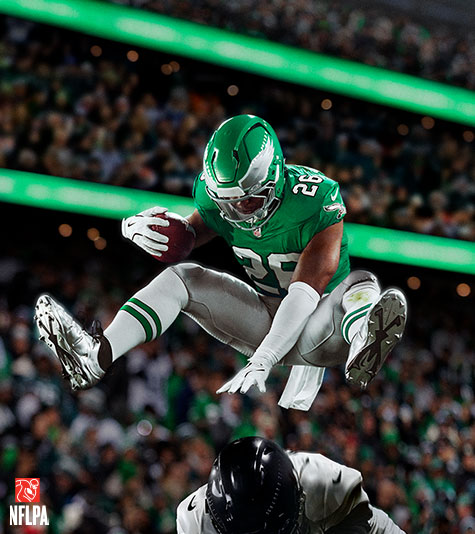 A Philadelphia Eagles football player leaping over another player with a football in hand.