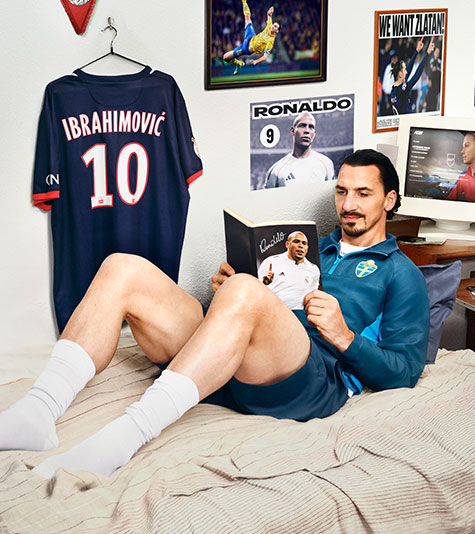 A soccer player lounging in his bed reading a magazine.