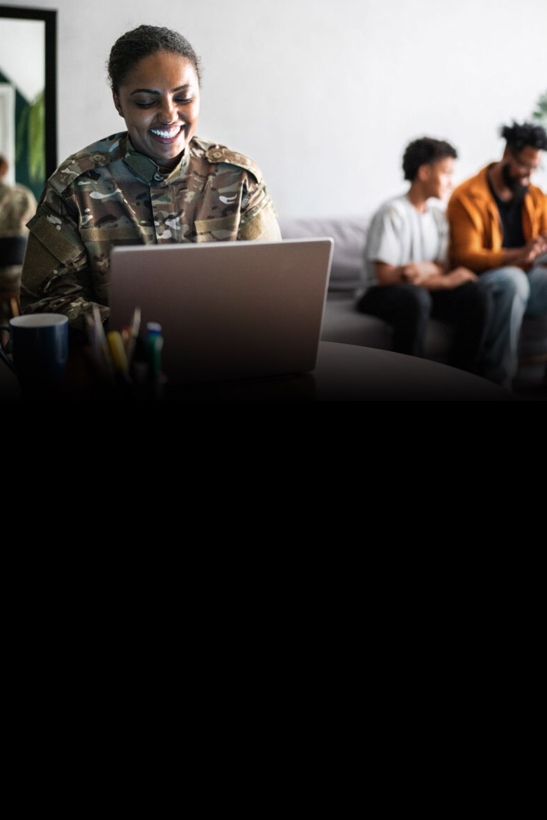 A person in a military uniform smiling joyfully at their laptop.