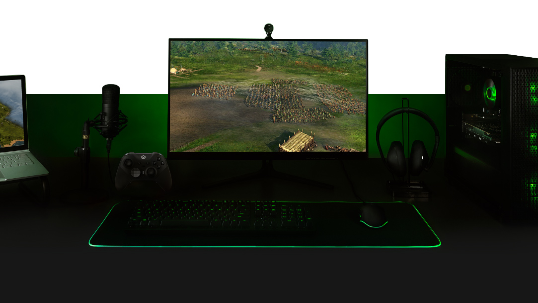 Desktop with a PC, monitor with Ara: History Untold game screen, keyboard, Xbox One controller, microphone and a laptop all set up together.