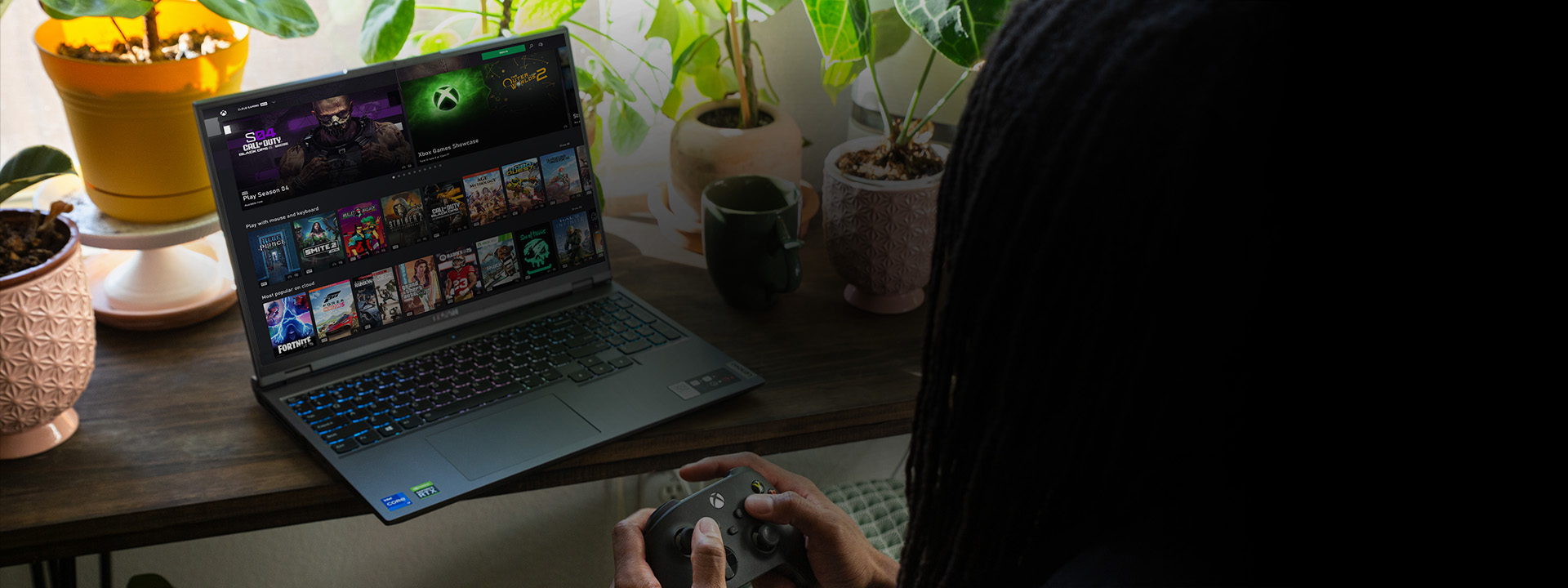 An over the shoulder view of a person holding a black Xbox Wireless Controller navigating the Xbox app on a laptop.