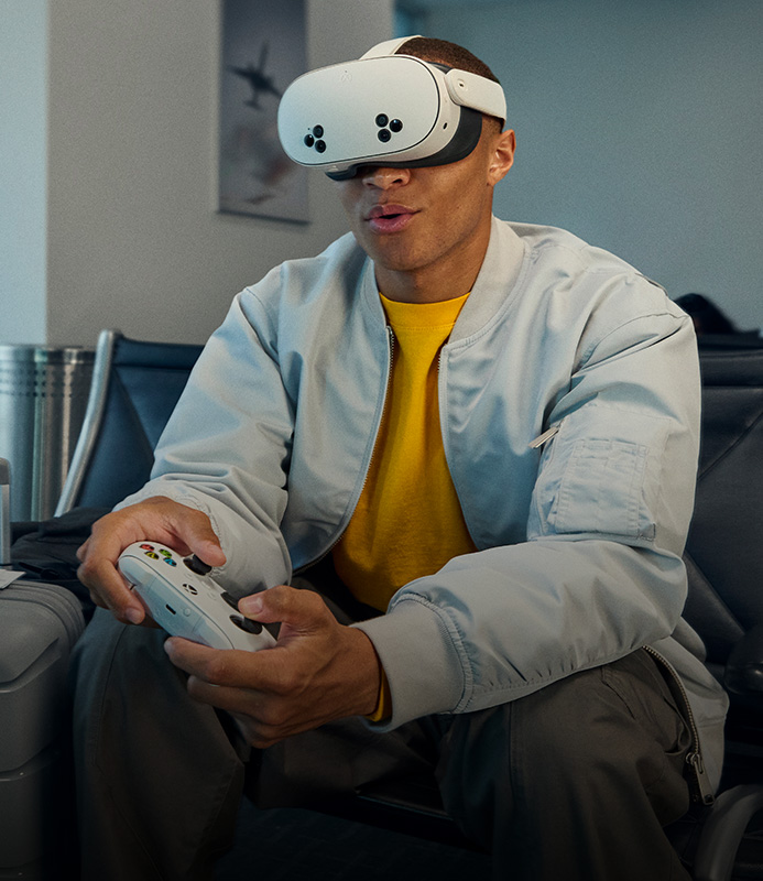 A person sitting in a chair holding a white Xbox Wireless Controller wearing a Meta Quest VR headset.