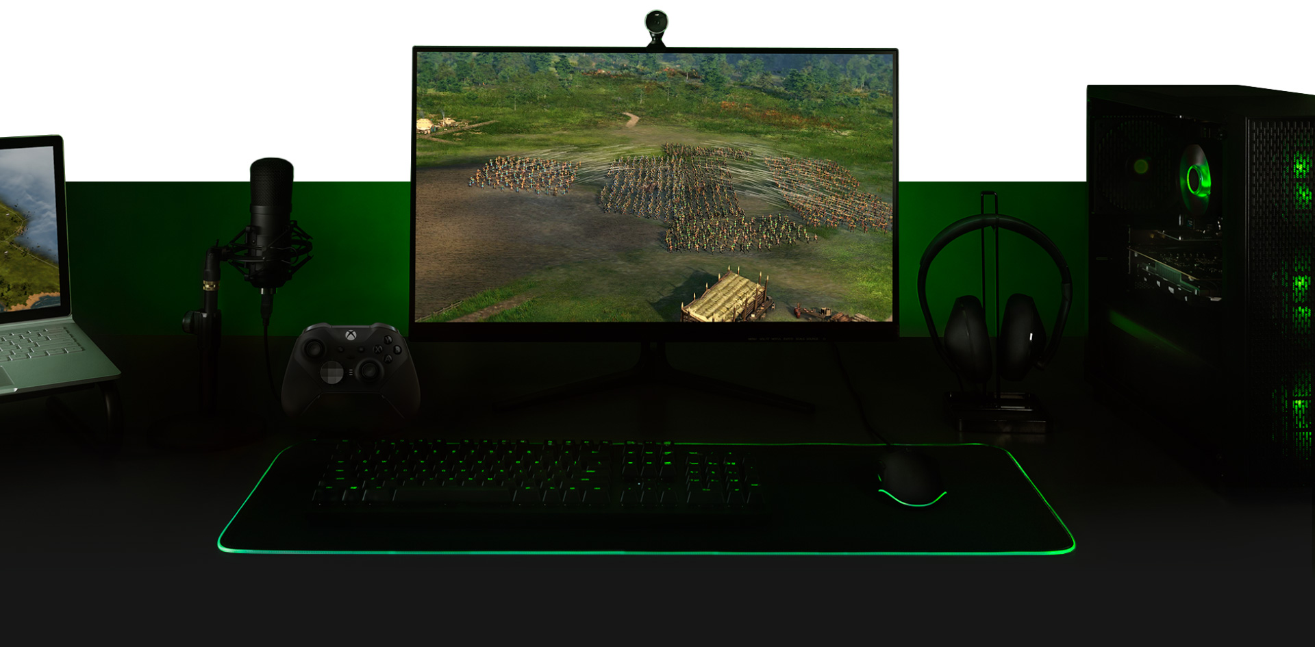 Desktop with a PC, monitor with Ara: History Untold game screen, keyboard, Xbox One controller, microphone, and a laptop all set up together.