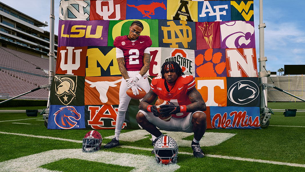 American football players posing on a football field in front of a banner featuring dozens of US college team logos.